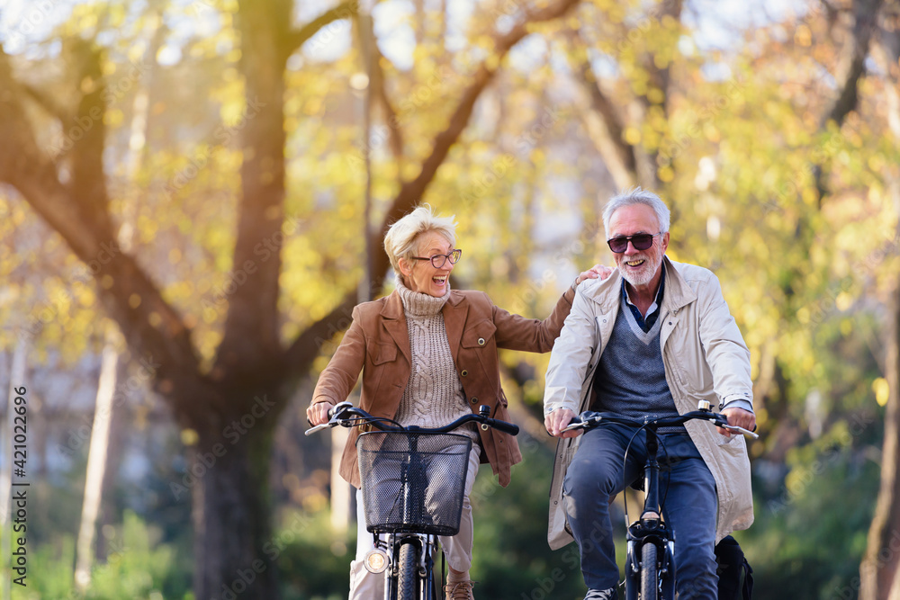 Cheerful active senior couple with bicycle in public park together having fun. Perfect activities for elderly people. Happy mature couple riding bicycles in park